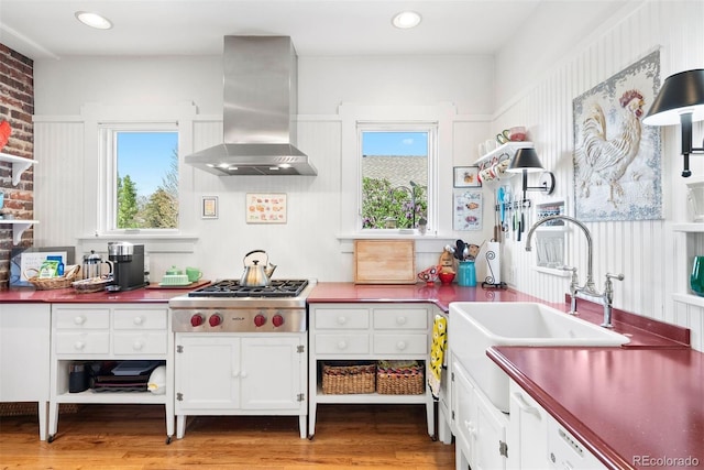 kitchen featuring exhaust hood, a sink, white cabinetry, stainless steel gas stovetop, and light wood-type flooring