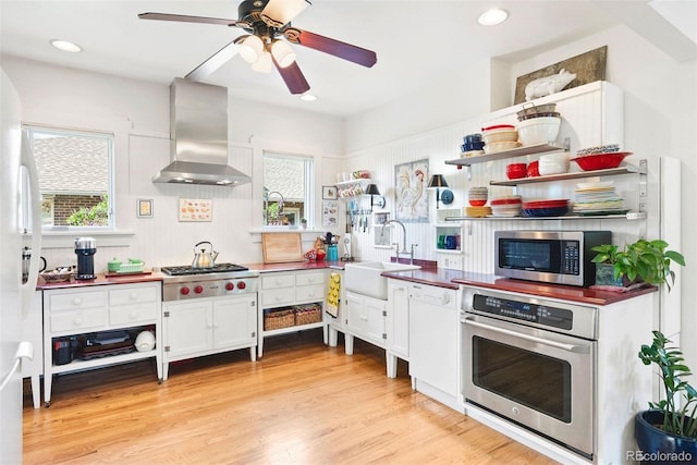 kitchen with wall chimney range hood, ceiling fan, open shelves, appliances with stainless steel finishes, and a sink