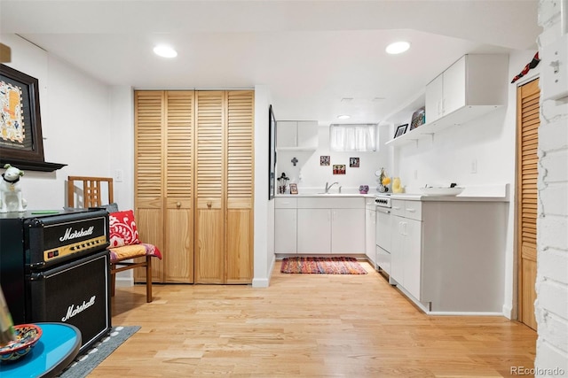 kitchen with open shelves, a sink, light wood-style floors, light countertops, and white cabinetry