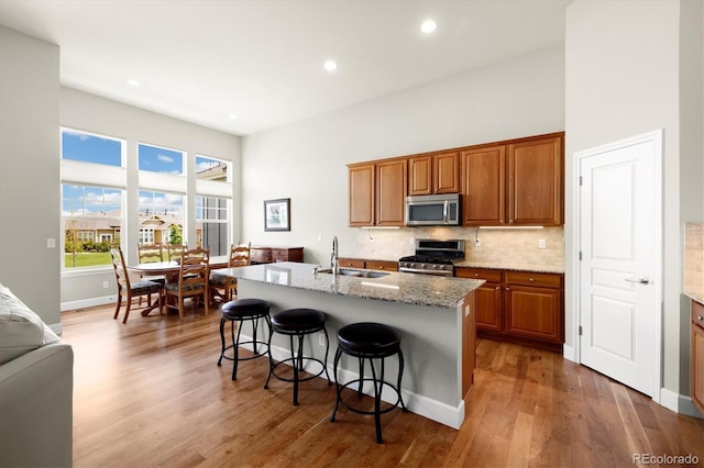14443 W 88th Dr Unit B, Arvada, CO 80005 - kitchen featuring appliances with stainless steel finishes, brown cabinetry, a kitchen breakfast bar, a towering ceiling, and wood finished floors