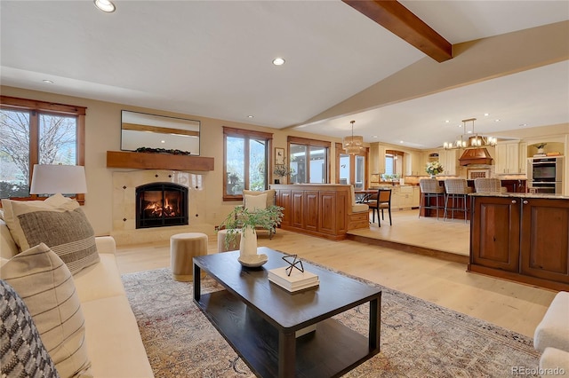 living room with a high end fireplace, vaulted ceiling with beams, a chandelier, and light hardwood / wood-style flooring