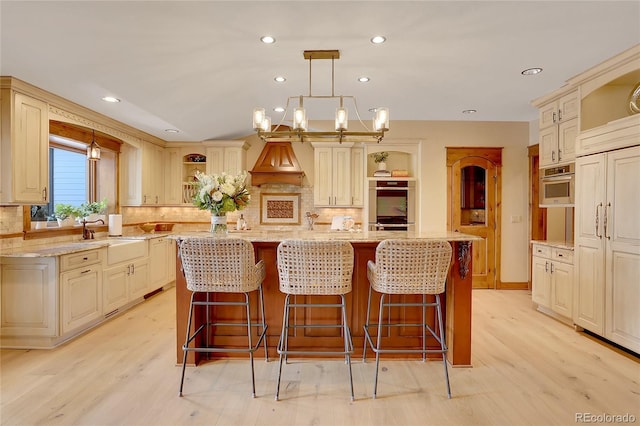 kitchen featuring a kitchen island with sink, decorative light fixtures, and cream cabinetry