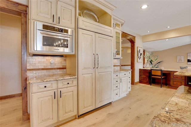 kitchen featuring decorative backsplash, light hardwood / wood-style floors, light stone countertops, and stainless steel oven