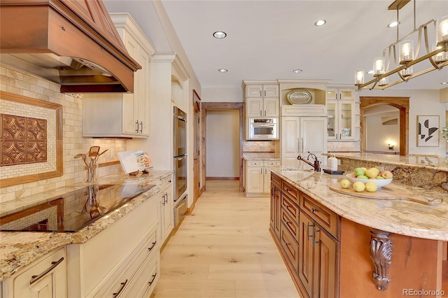 kitchen with sink, light stone counters, premium range hood, backsplash, and pendant lighting