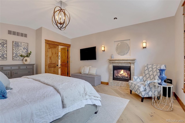 bedroom featuring a premium fireplace, light wood-type flooring, vaulted ceiling, and an inviting chandelier