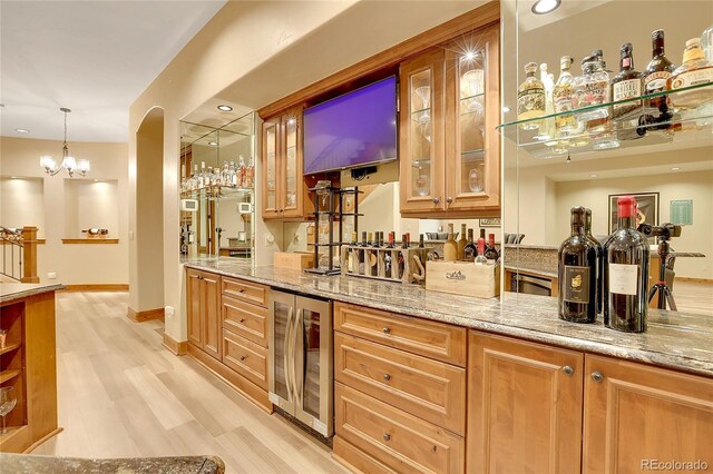 bar featuring pendant lighting, light hardwood / wood-style flooring, light stone counters, beverage cooler, and a chandelier