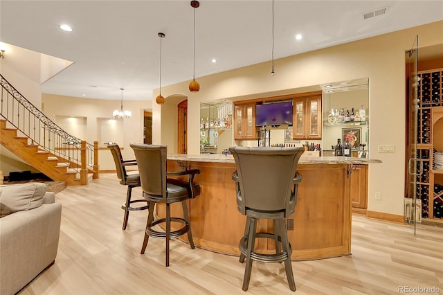 bar with a chandelier, pendant lighting, light wood-type flooring, and light stone counters