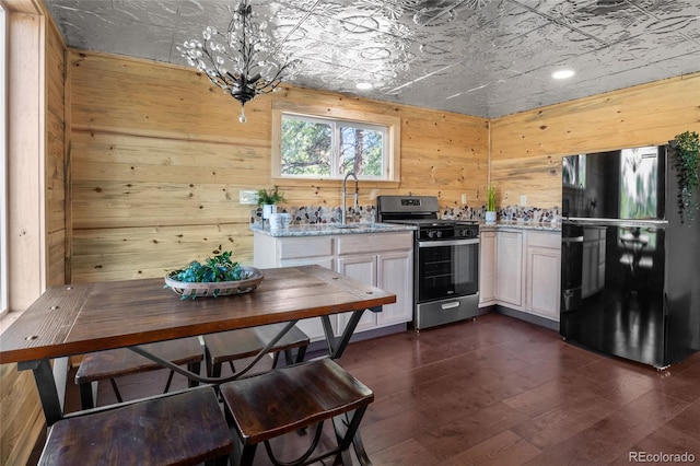 kitchen featuring dark hardwood / wood-style floors, sink, stainless steel range, wooden walls, and black fridge