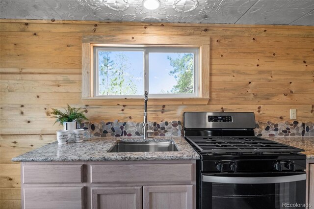 kitchen featuring sink, light stone counters, wood walls, and stainless steel gas range oven