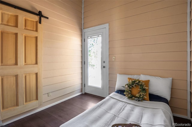 bedroom with multiple windows, wooden walls, dark hardwood / wood-style floors, and a barn door