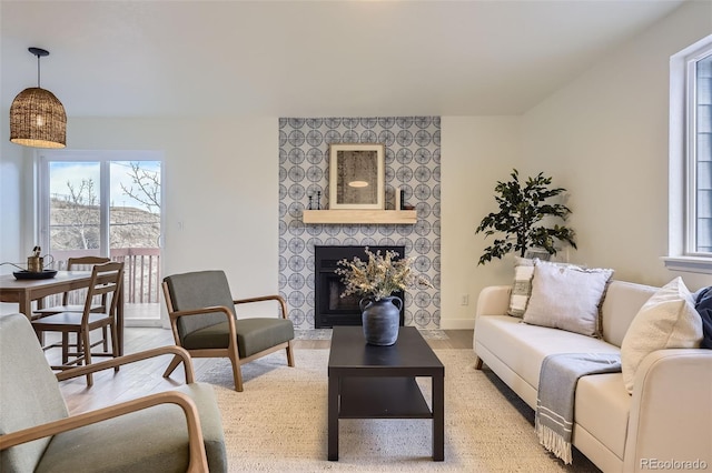 living room with plenty of natural light, a tiled fireplace, light wood-style flooring, and baseboards