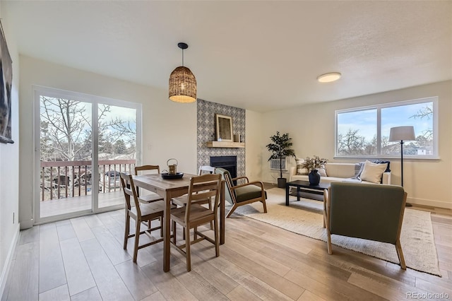 dining space with a large fireplace, light wood-style flooring, and baseboards