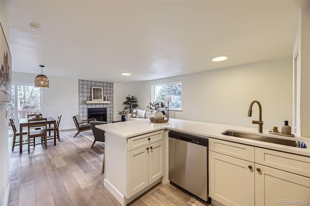 kitchen featuring a tile fireplace, a sink, light countertops, light wood-type flooring, and dishwasher