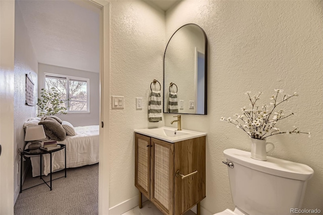 bathroom with toilet, vanity, and a textured wall