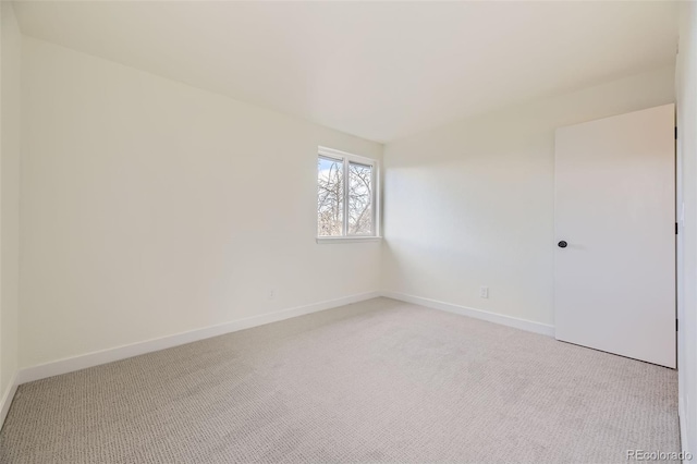 spare room featuring light carpet and baseboards