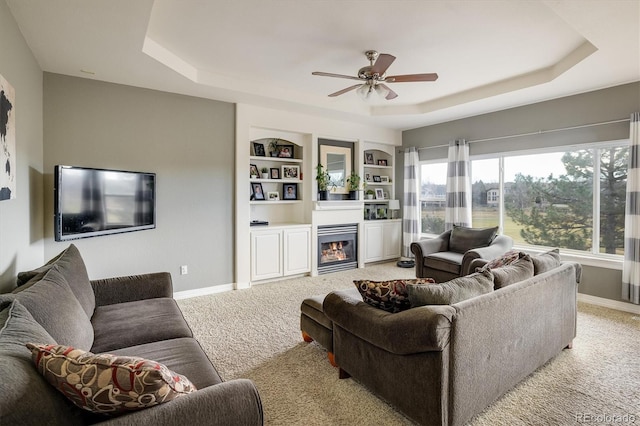 living room featuring light carpet, built in shelves, a raised ceiling, and ceiling fan