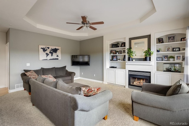 carpeted living room with built in shelves, a tray ceiling, and ceiling fan