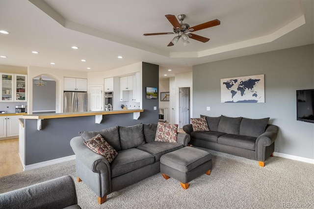 carpeted living room featuring a raised ceiling and ceiling fan