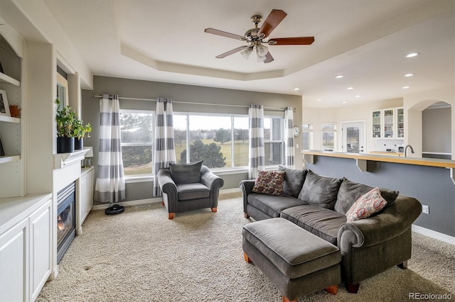 carpeted living room with a tray ceiling and ceiling fan