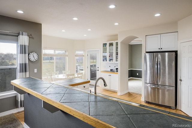 kitchen with tile countertops, stainless steel fridge, light wood-type flooring, and white cabinetry