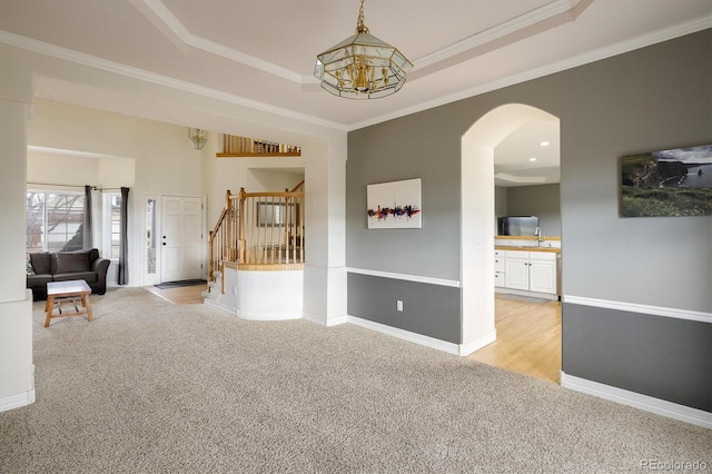 interior space with light carpet, a raised ceiling, ornamental molding, and a notable chandelier