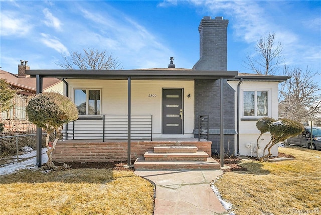 view of front facade with a porch, a chimney, and a front lawn