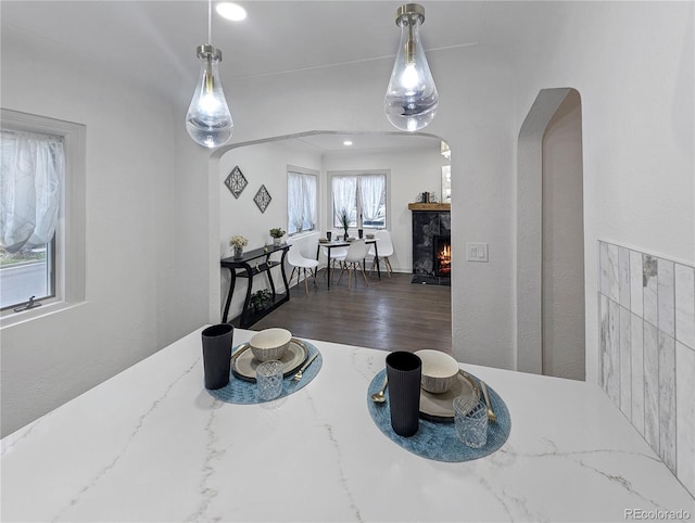 interior space featuring a warm lit fireplace, arched walkways, and wood finished floors