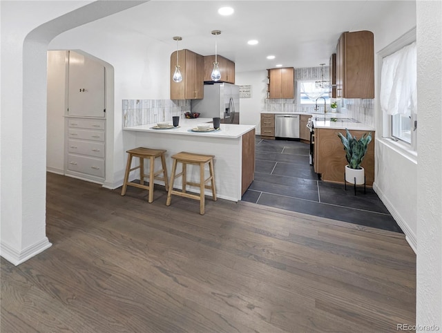 kitchen featuring a peninsula, decorative backsplash, stainless steel appliances, and brown cabinets