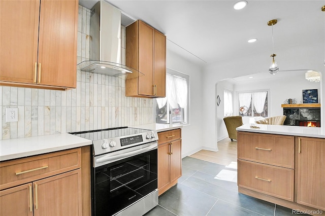 kitchen featuring stainless steel electric range oven, hanging light fixtures, decorative backsplash, wall chimney range hood, and light countertops