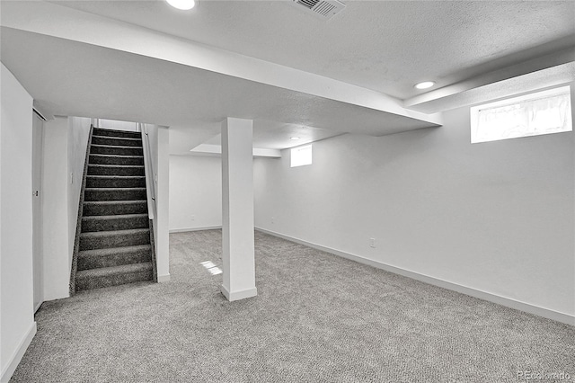 below grade area featuring stairs, a textured ceiling, visible vents, carpet flooring, and baseboards