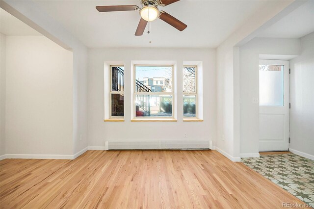 empty room featuring light wood finished floors, a baseboard heating unit, baseboards, and a ceiling fan