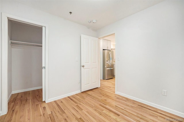 unfurnished bedroom with a closet, light wood finished floors, baseboards, and stainless steel fridge