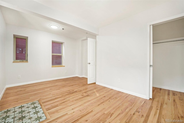 unfurnished bedroom featuring a spacious closet, a closet, baseboards, and light wood-type flooring