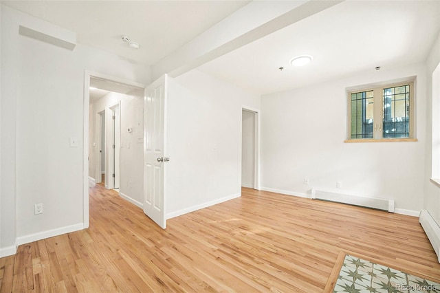 spare room featuring light wood finished floors, a baseboard heating unit, and baseboards