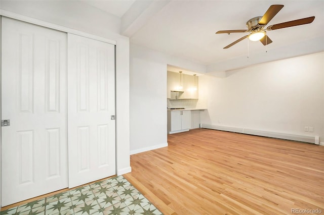 unfurnished living room featuring a baseboard heating unit, light wood finished floors, baseboards, and a ceiling fan