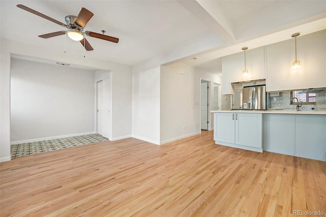 unfurnished living room with light wood-style flooring, a ceiling fan, a sink, baseboards, and beam ceiling