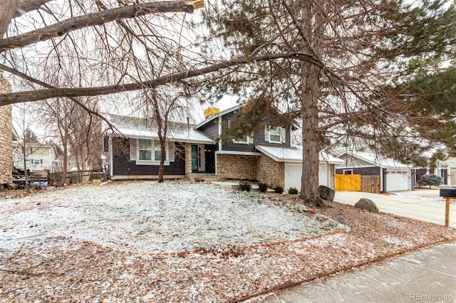 split level home featuring a garage, stone siding, fence, and concrete driveway