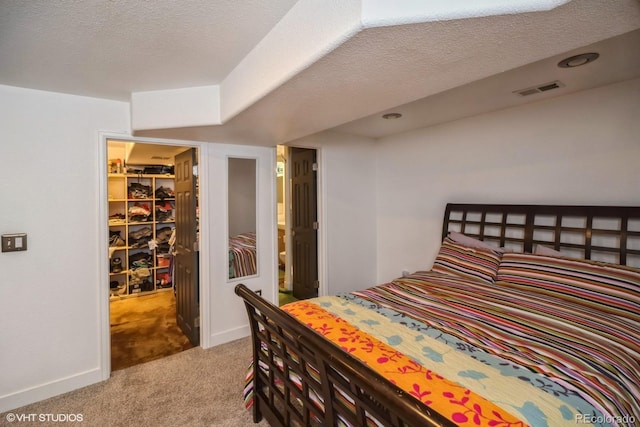 bedroom featuring visible vents, baseboards, a textured ceiling, a spacious closet, and carpet flooring