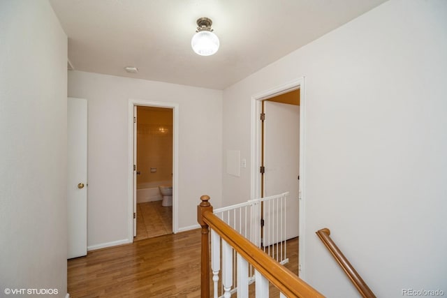 hall featuring baseboards, an upstairs landing, and light wood-type flooring