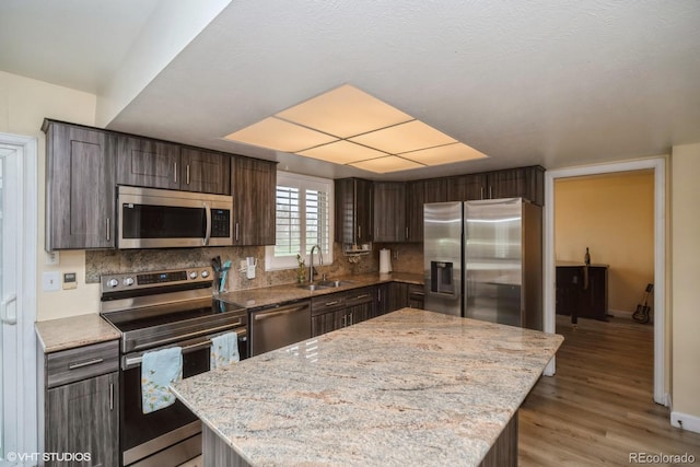 kitchen featuring dark brown cabinetry, light wood-style floors, tasteful backsplash, a sink, and stainless steel appliances