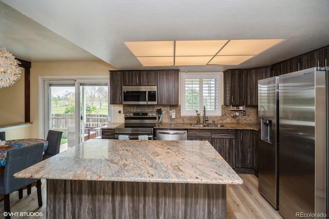 kitchen featuring dark brown cabinetry, backsplash, appliances with stainless steel finishes, light wood-type flooring, and a sink