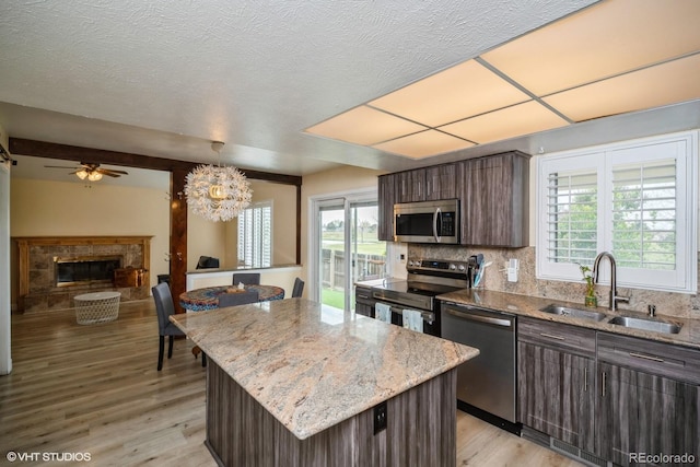 kitchen with appliances with stainless steel finishes, a sink, a fireplace with raised hearth, light wood-style flooring, and a kitchen island