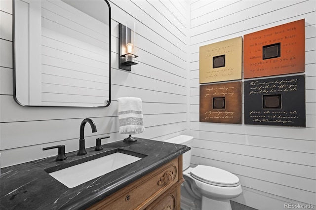 bathroom with wood walls, oversized vanity, and toilet