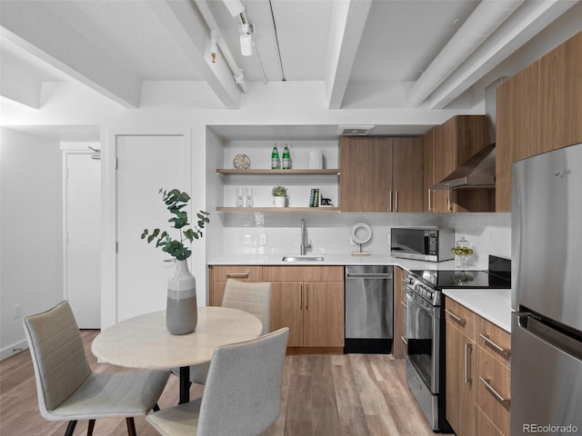 kitchen with wall chimney exhaust hood, appliances with stainless steel finishes, a sink, and light wood-style floors