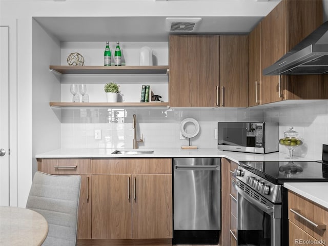 kitchen featuring a sink, light countertops, appliances with stainless steel finishes, wall chimney exhaust hood, and open shelves