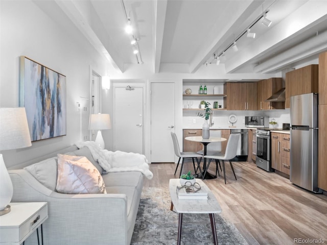 living area featuring track lighting, beamed ceiling, and light wood-style floors