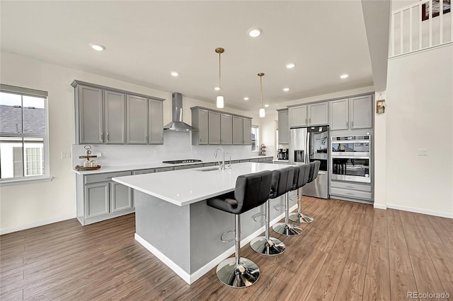 kitchen with a kitchen bar, wood-type flooring, hanging light fixtures, wall chimney range hood, and stainless steel appliances