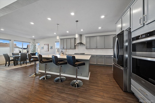 kitchen featuring appliances with stainless steel finishes, gray cabinetry, wall chimney exhaust hood, and an island with sink