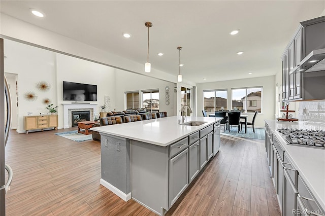 kitchen featuring hanging light fixtures, sink, gray cabinetry, an island with sink, and stainless steel gas cooktop