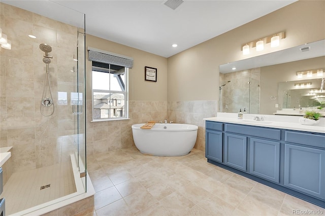 bathroom with tile walls, tile patterned floors, vanity, and plus walk in shower